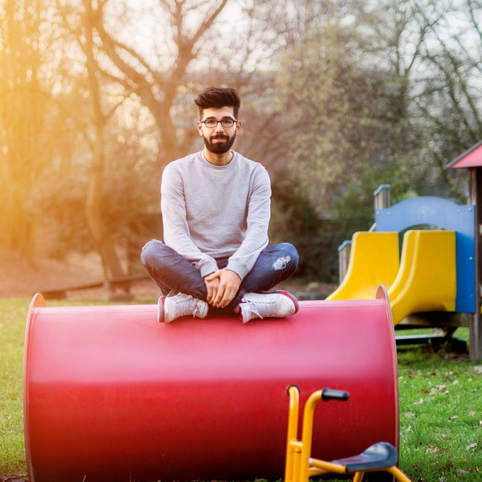 Junger Mann sitzt auf einem Rohr auf einem Spielplatz und lächelt